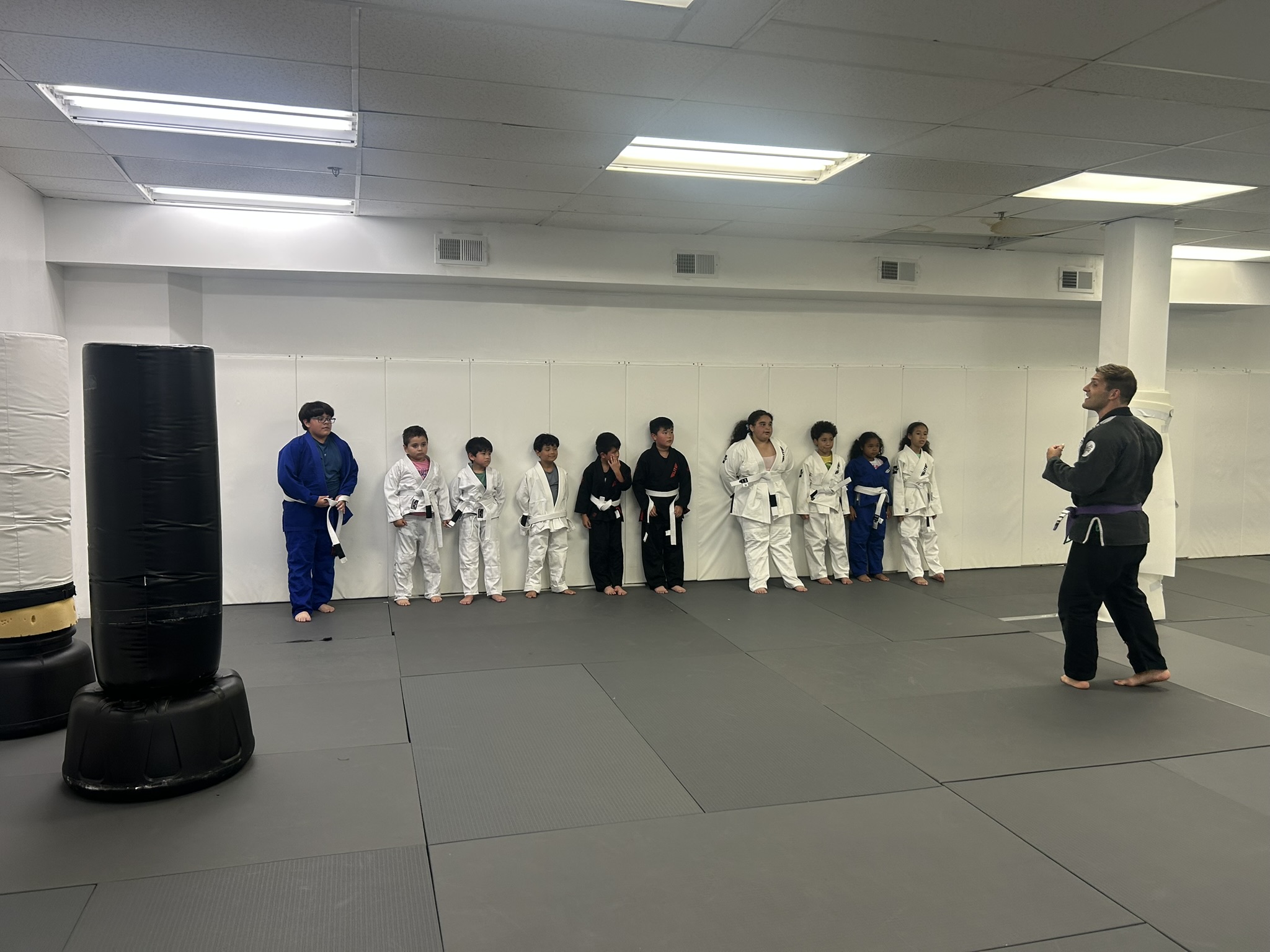 A line of kids in their gis standing on the mats as an Immortals coach leads the start of a kids jiu jitsu class.