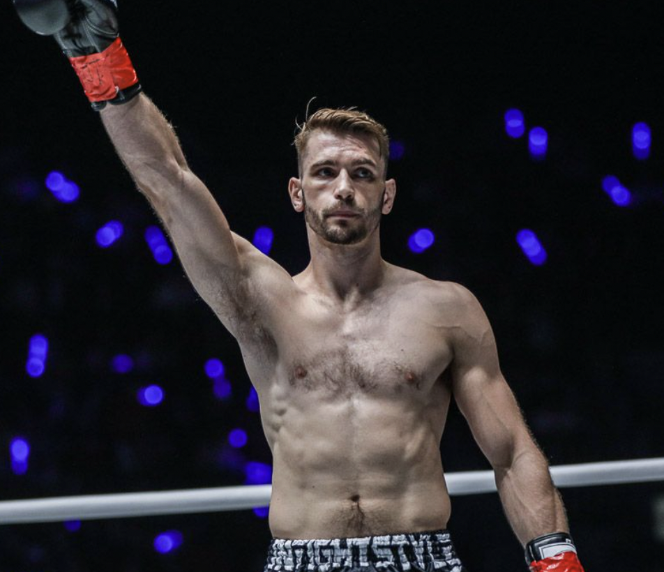 Ognjen Topic, Muay Thai head instructor at Immortals, raising a gloved arm in victory in the ring.